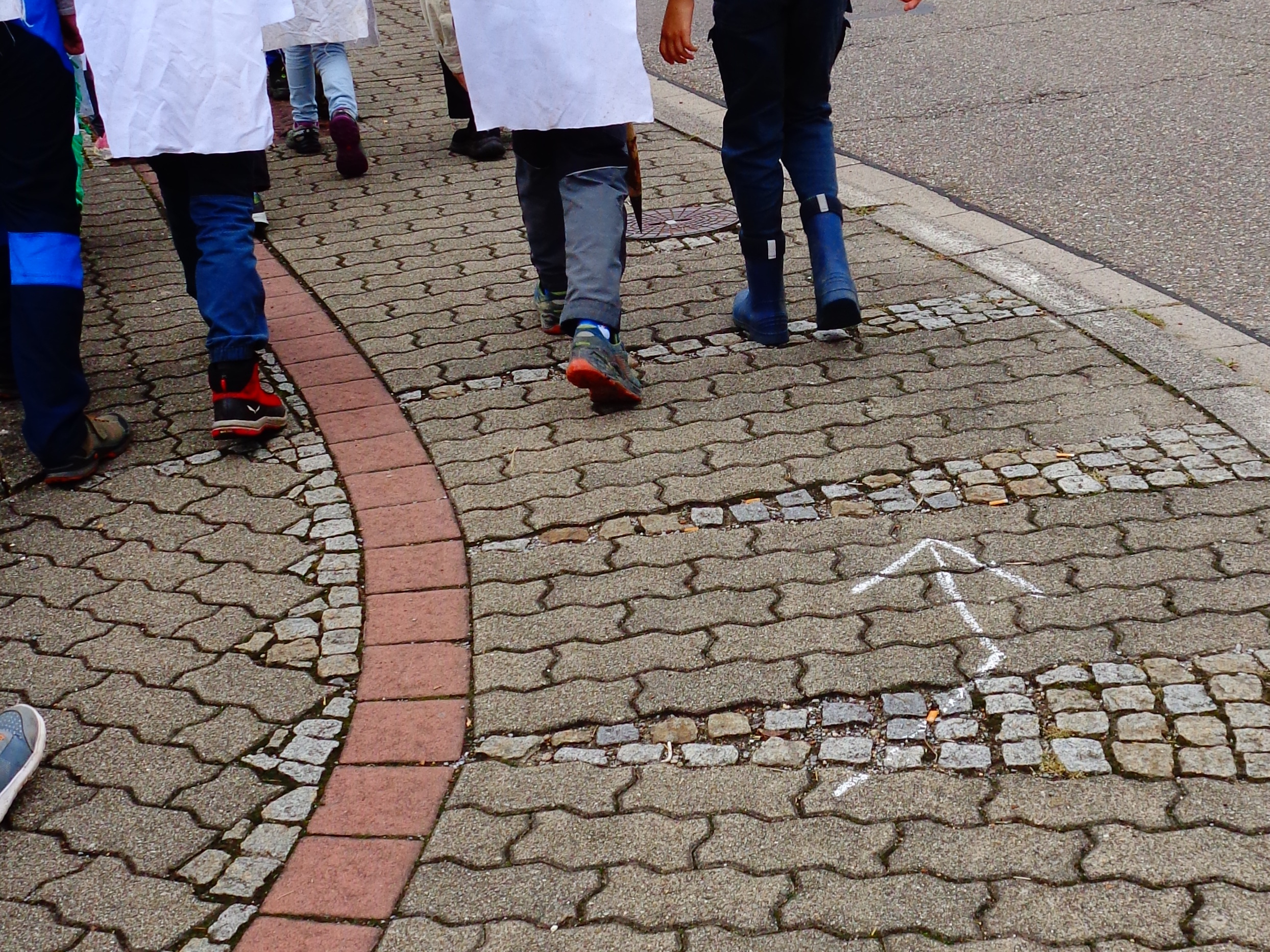Pfadfinder laufen an einer Straße auf dem Gehsteig entlang und folgen einer Spur aus Kreidezeichen