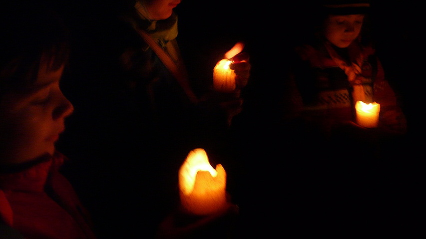 Drei Jungen der Meute Biber schützen die Kerzenflamme vor dem Wind mit der Hnad