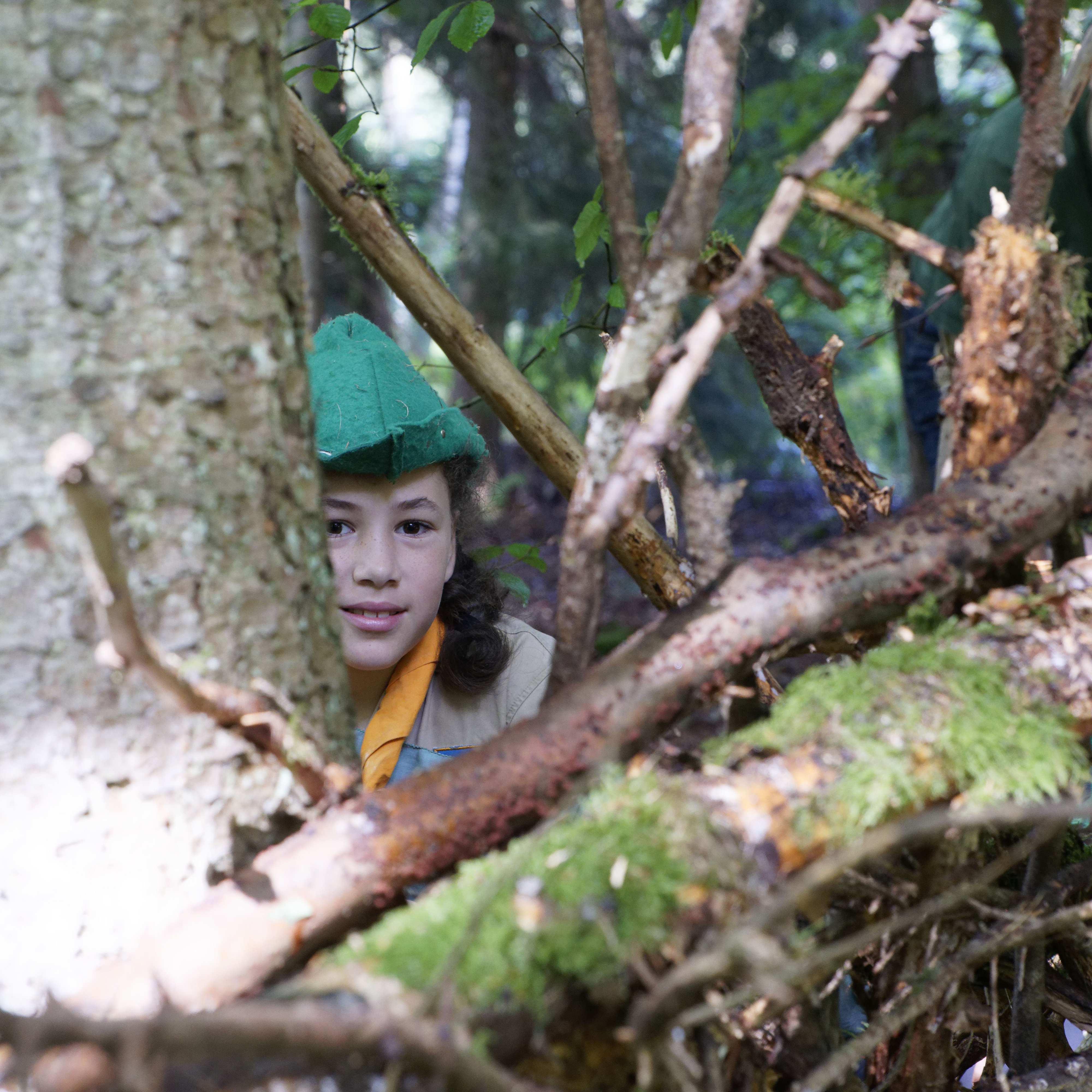 Eine junge Pfadfinderin trägt beim Verstecken einen grünen Hut