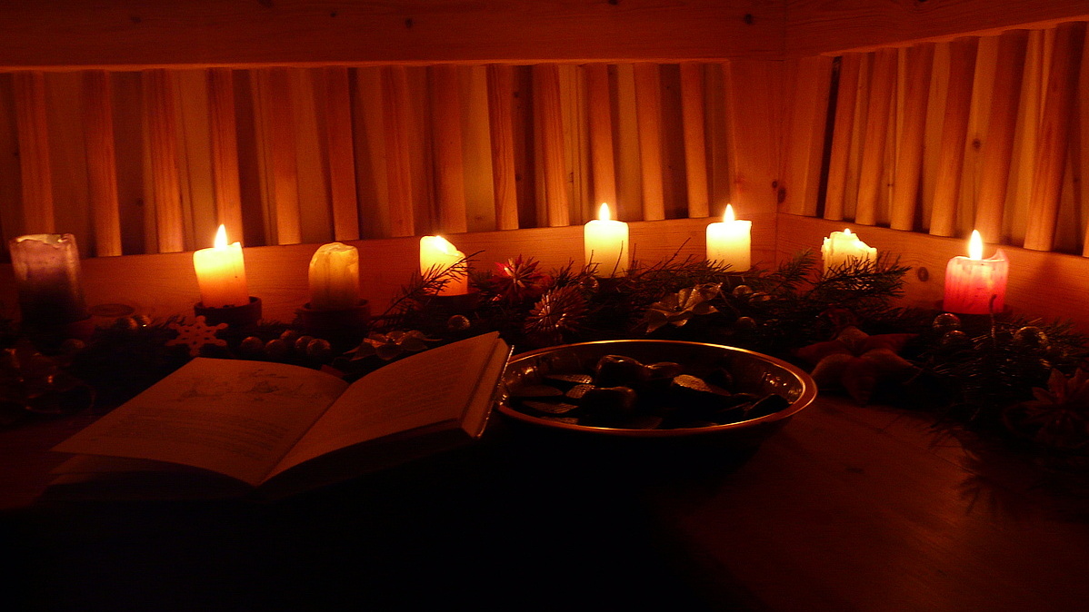 Auf einer Holzbank in der Waldhütte sind Kerzen und Tannenreisig drapiert.
