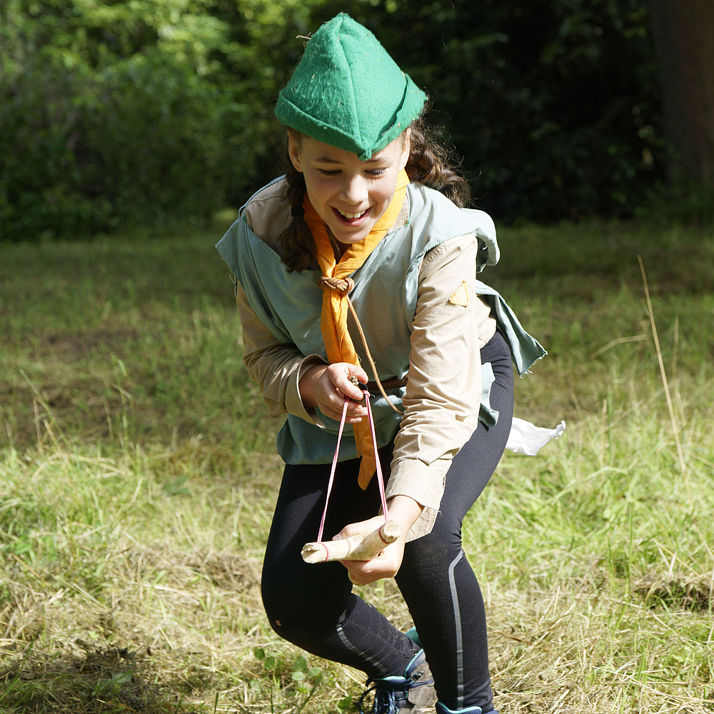 Ein Mädchen im Robin Hood Gewand schießt mit der Zwille