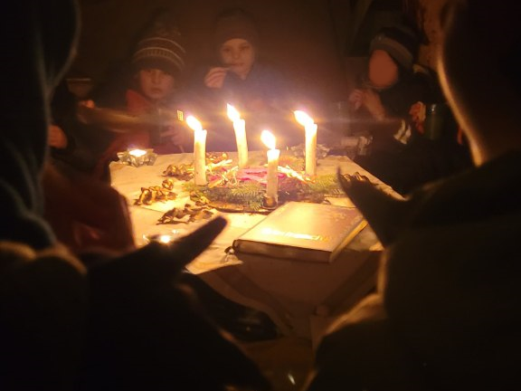 Um einen Adventskranz sitzen die Kinder und essen Plätzchen