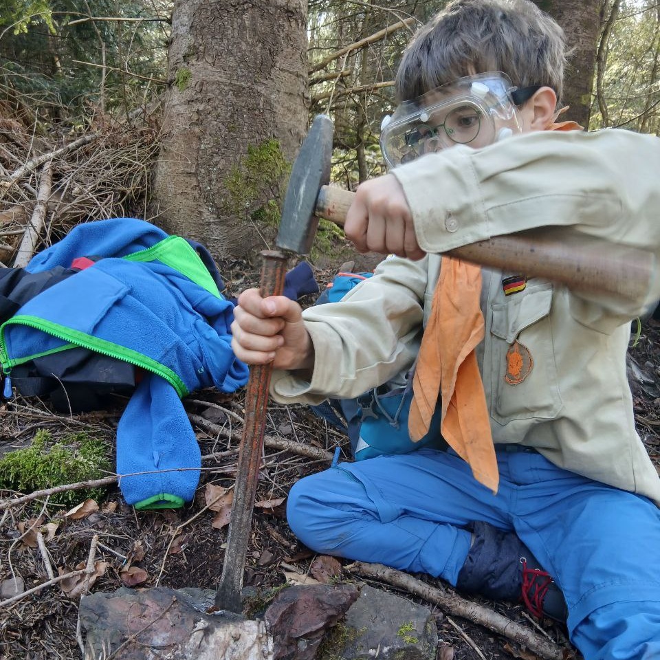 Ein Wölfling schlägt mit dem Hammer kräftig auf das Gestein