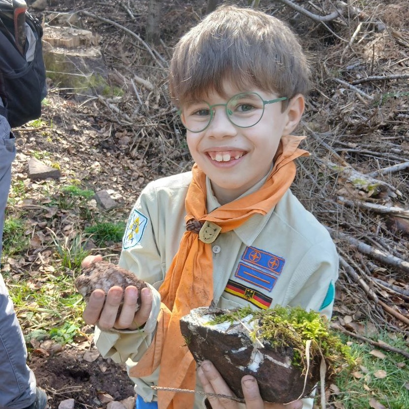 Zwei schwere Steinbrocken im Arm lacht dieser Junge 