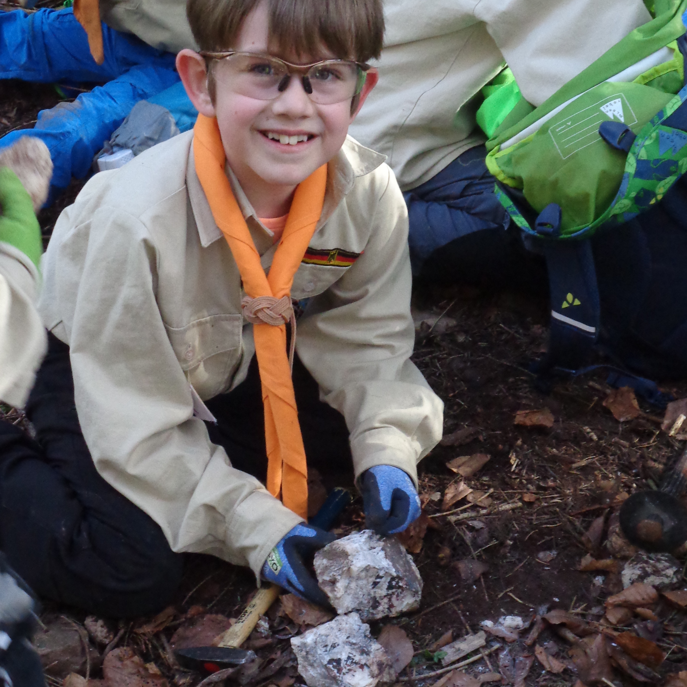 Fröhlich lacht der junge Pfadfinder beim Steinebearbeiten in die Kamera