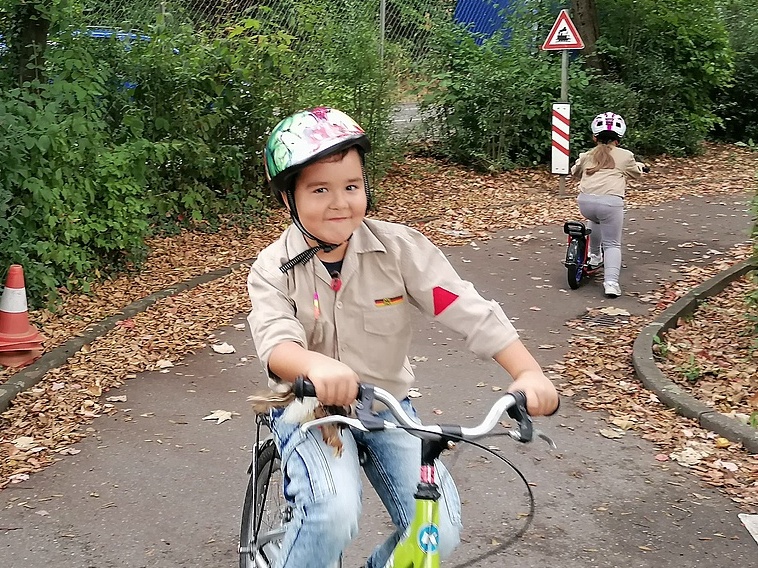 Ein kleiner Pfadfinder lacht im Vorbeifahren in die Kamera