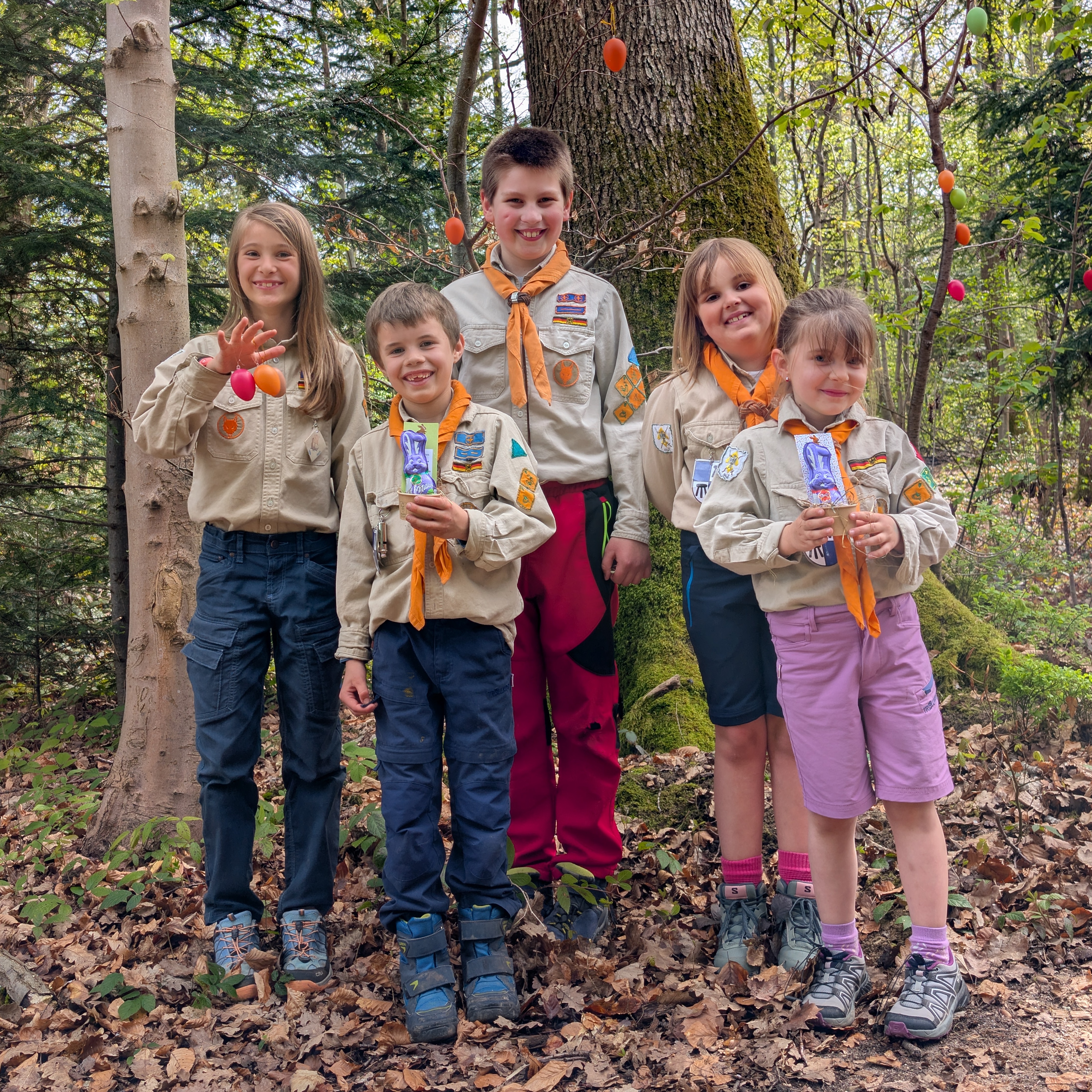 Mädchen und Jungen aus der Meute lachen bei der Eiersuche in die Kamera