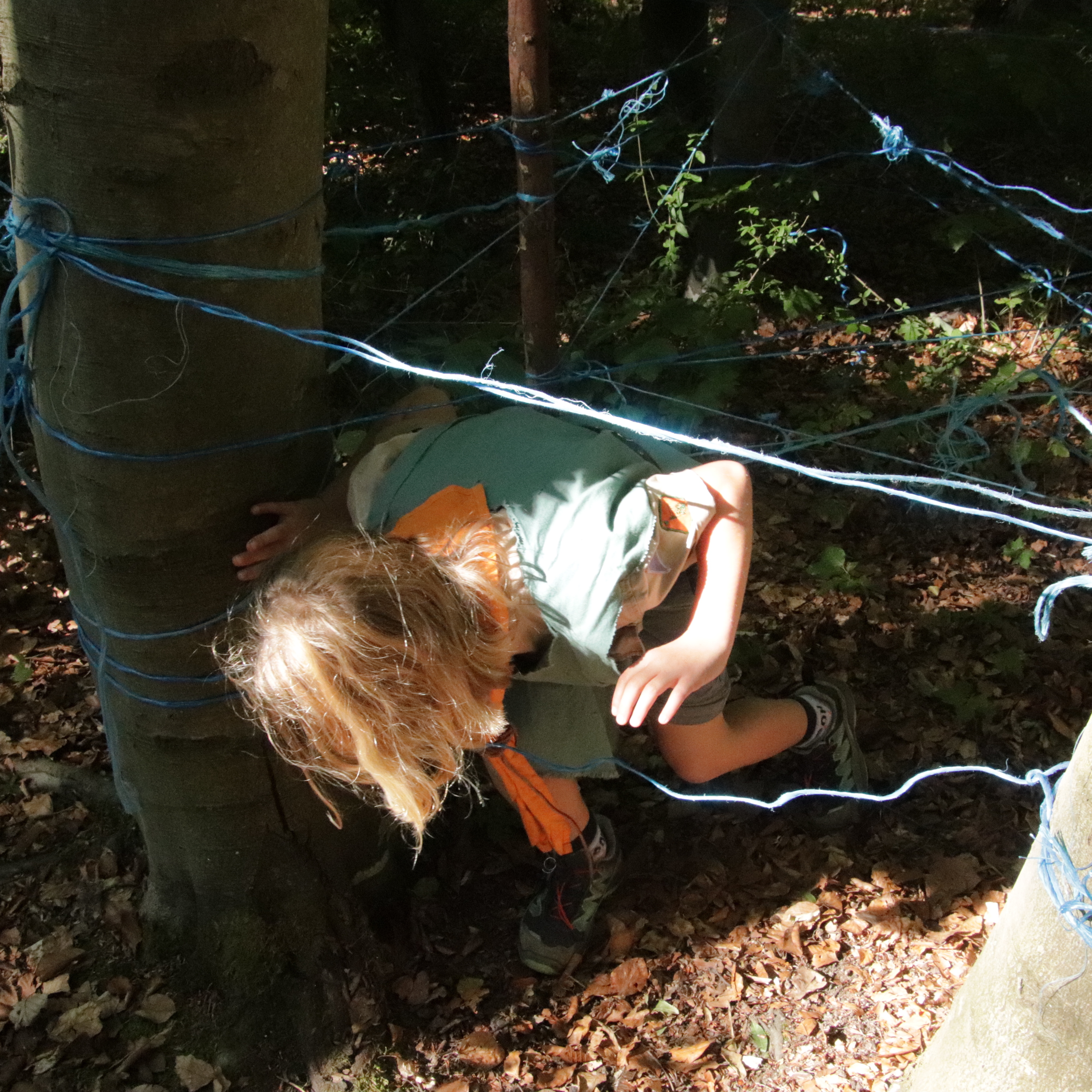 Geschickt klettert das Mädchen durch das Spinnennetz Ein Mädchen klettert durch einen Hindernissparcours aus Schnüren
