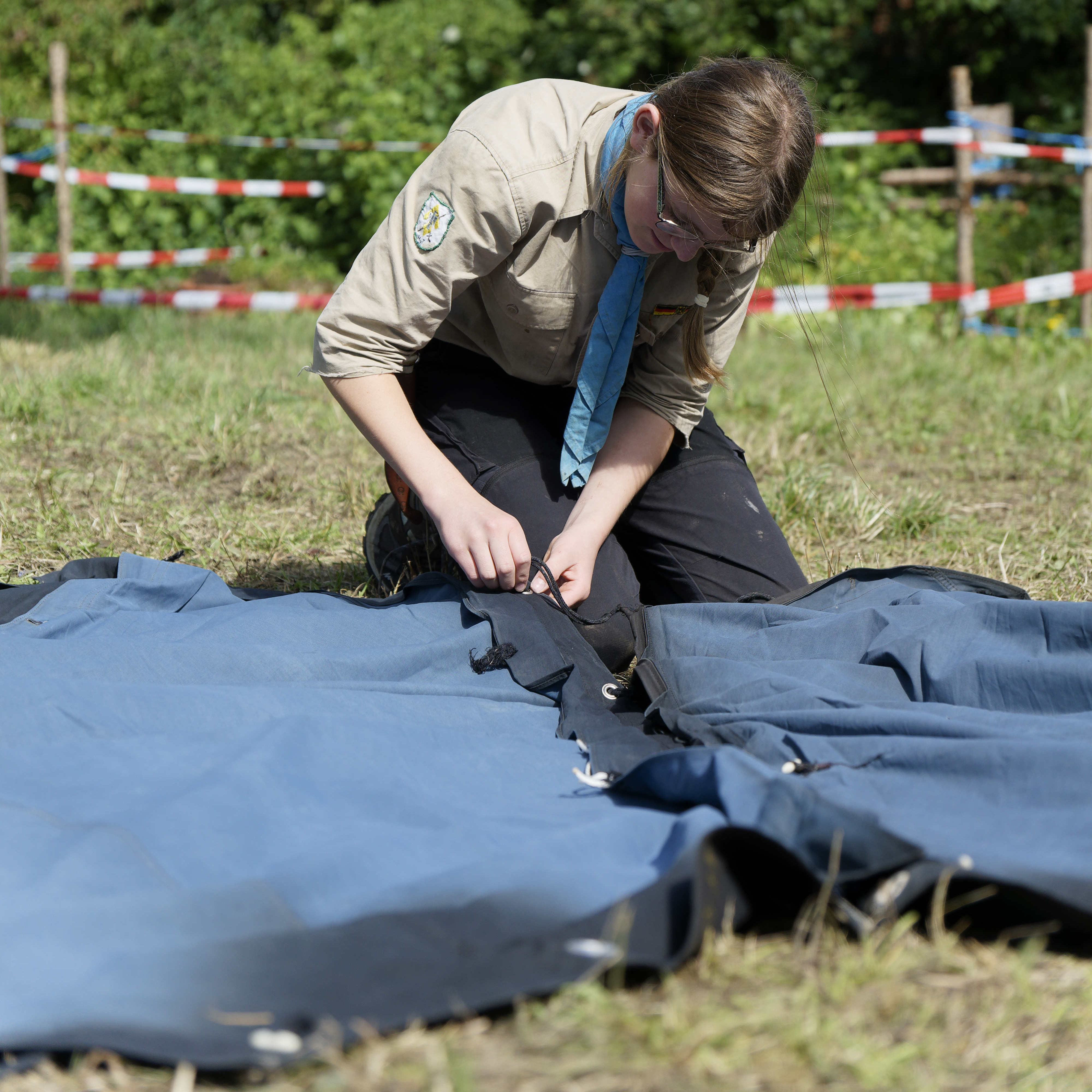 Eine Pfadfinderin knüpft zwei Zeltbahnen zusammen für den Aufbau eines Zeltes