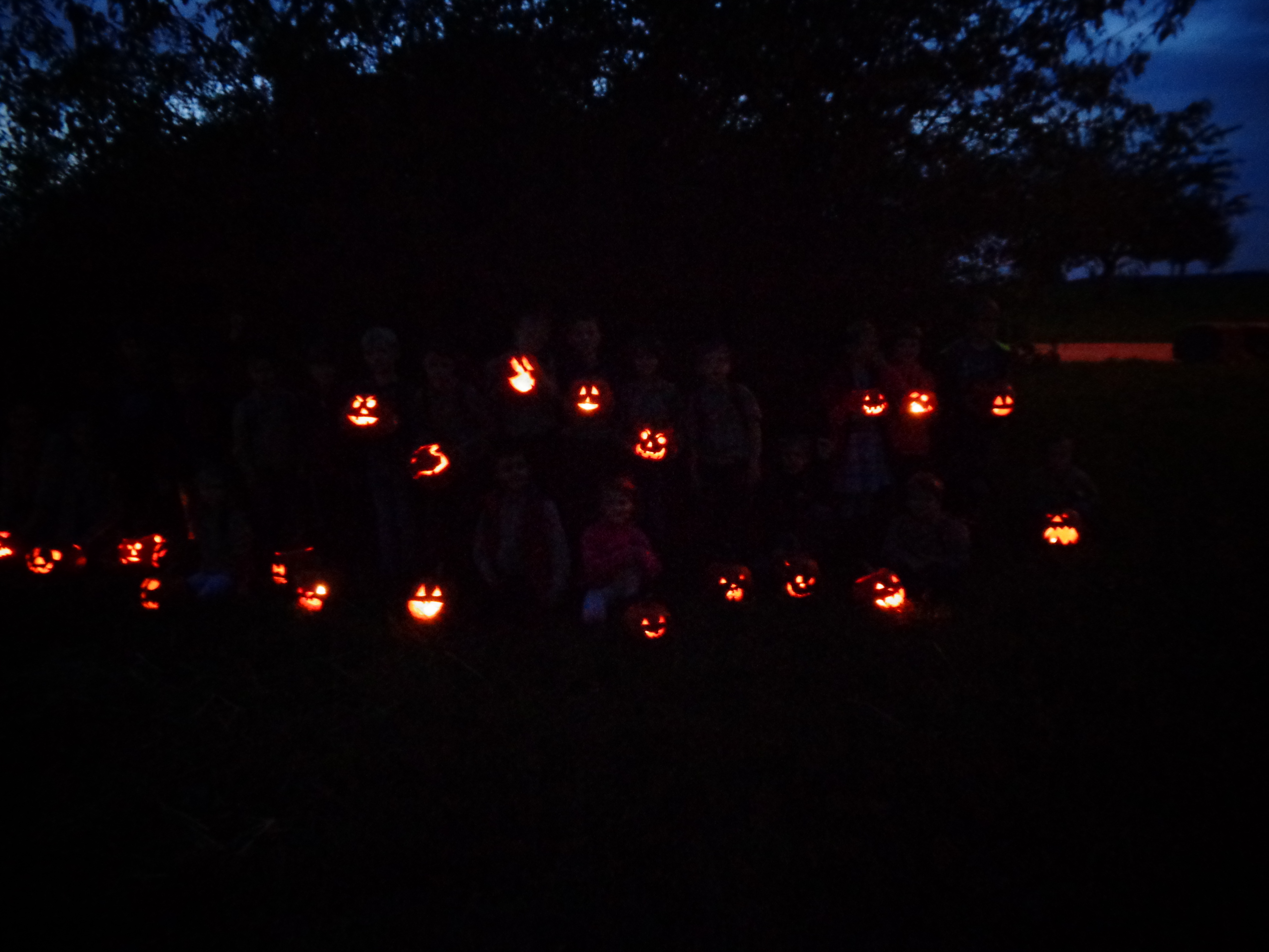 Eine große Gruppe Pfadfinder steht im Dunkeln mit ihren leuchtenden Kürbissen